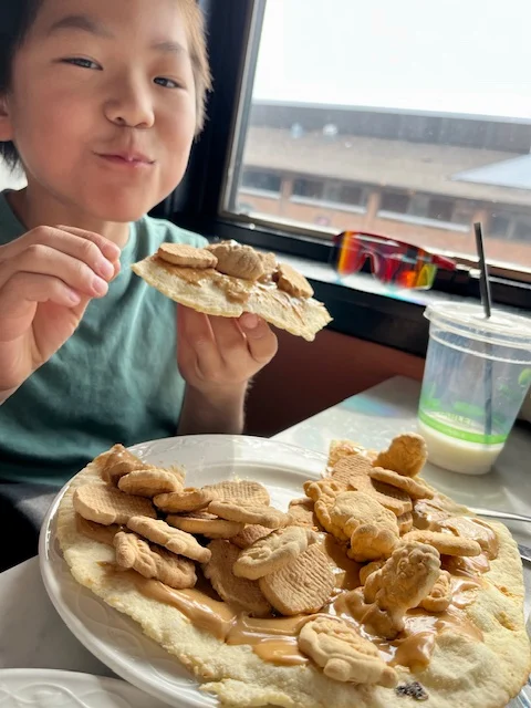 boy smiling while chewing - holding pizza covered in peanut butter and animal crackers