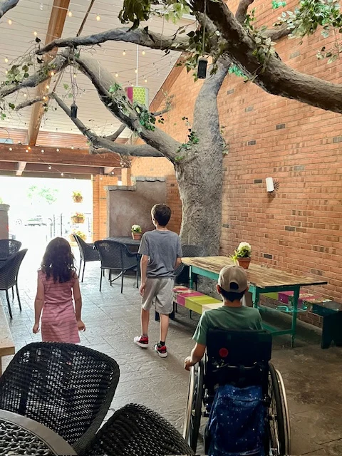 three children strolling through fake trees and picnic tables at restaurant entrance