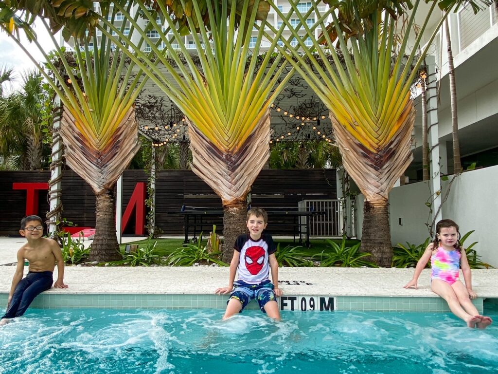 three children splashing in pool in front of palm trees