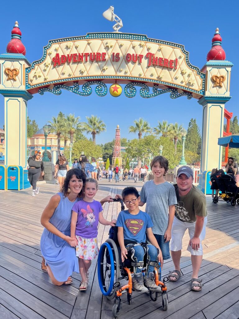 family in disney california adventure park in front of "adventure is out there" sign