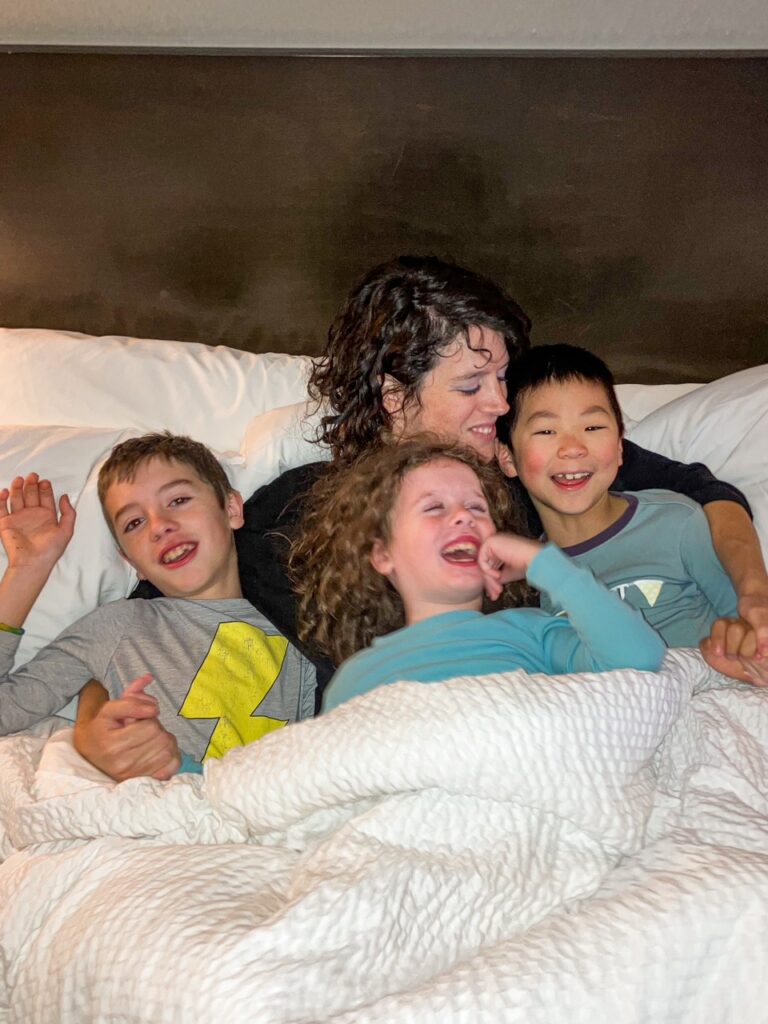 mom snuggling kids in bed
