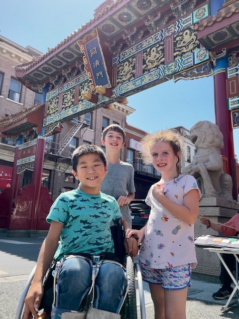 three children, one in a wheelchair, in front of chinese gate