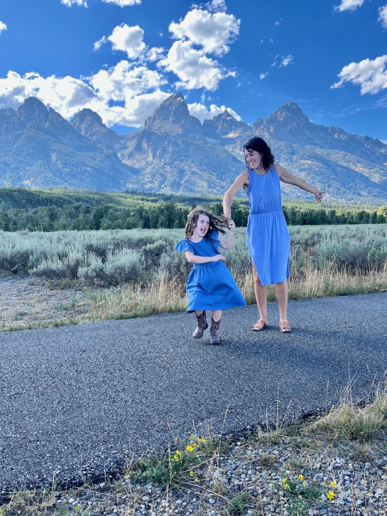 mom spinning little girl on paved path with mountains in the background