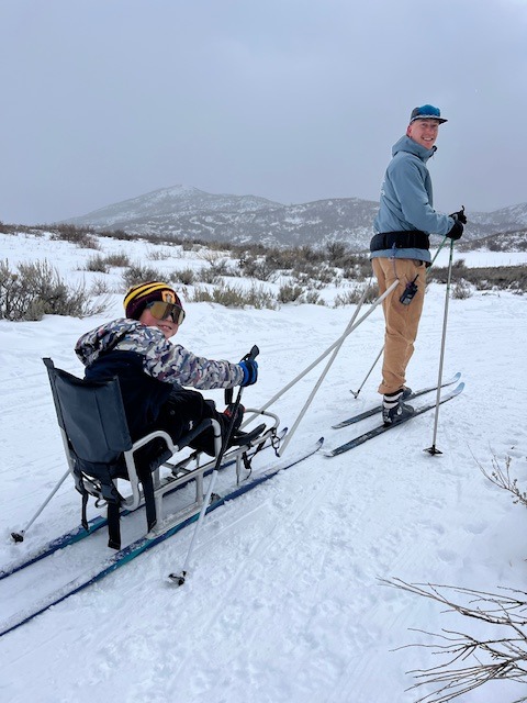 boy in adaptive nordic sled being pulled by man on cross country skis