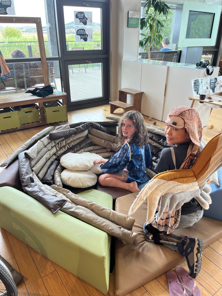 little girl and little boy in a foam bird's nest that they built. Little boy is wearing an owl costume. Both children are smiling at the camera.