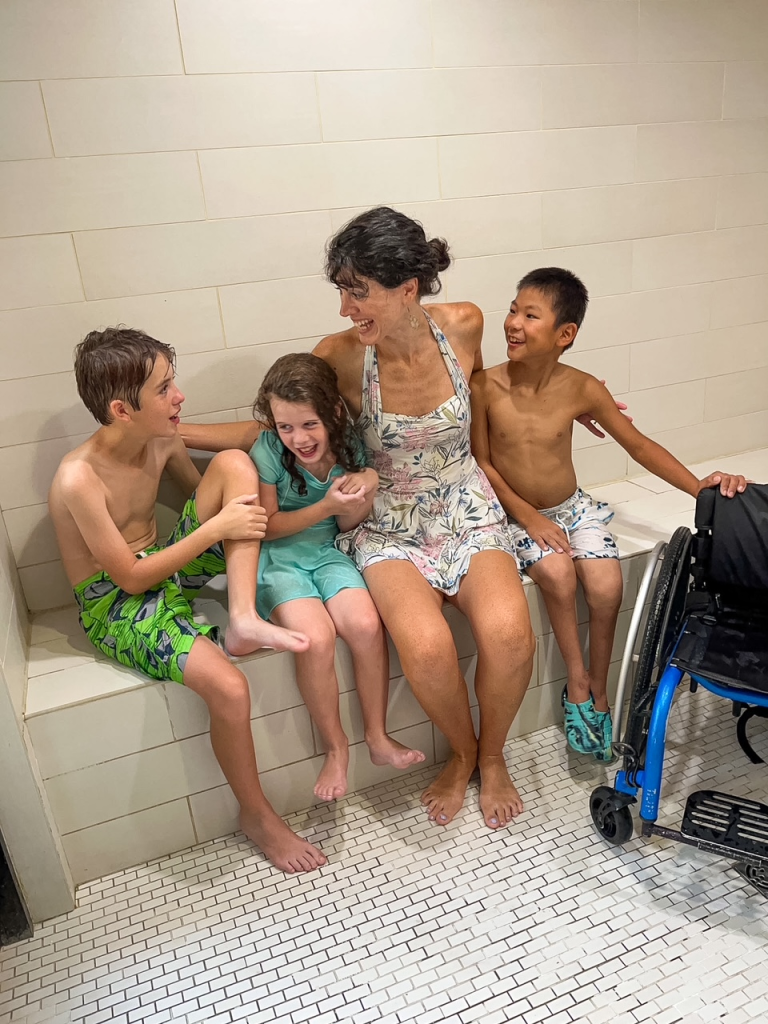 three kids and mom laughing in steam room. wheelchair parked on the side.