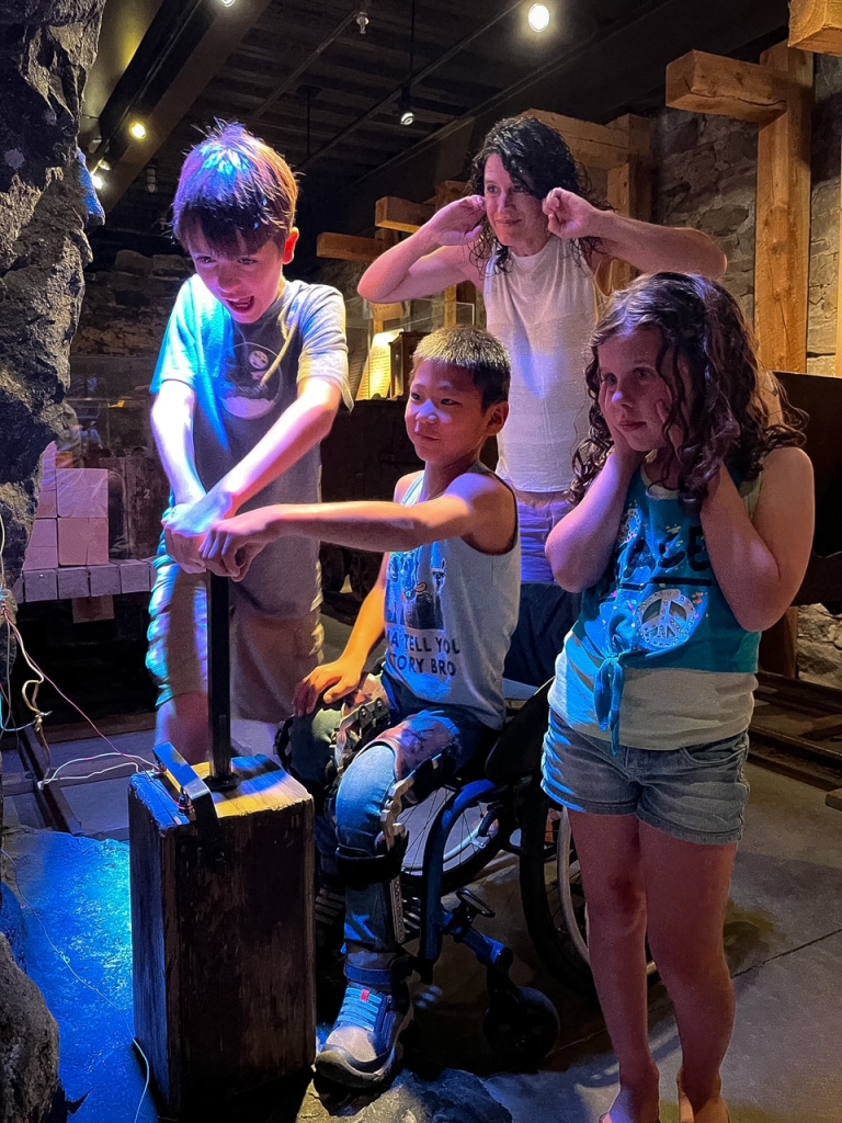 Two boys push down the handle to blow the dynamite while mom and sister hold their ears