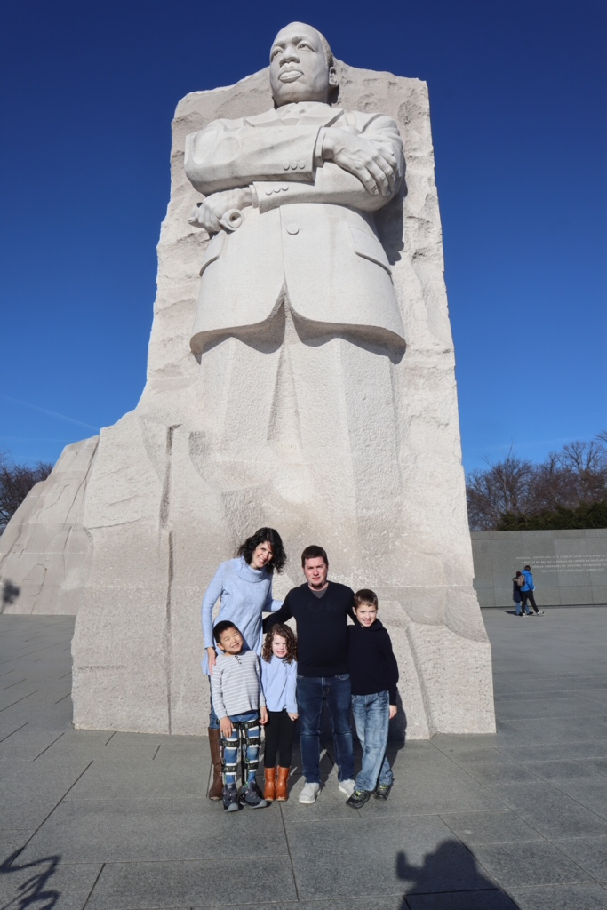 Family smiles for camera in front of massive pale sculpture of MLK Jr