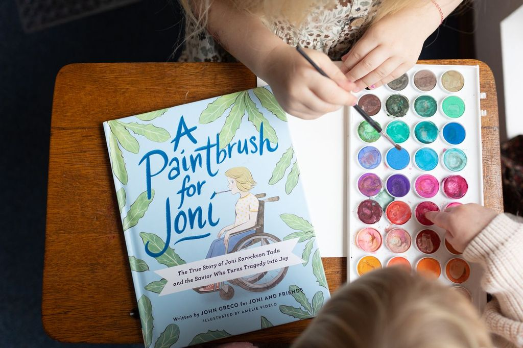 Cover of A Paintbrush for Joni next to children's hands painting