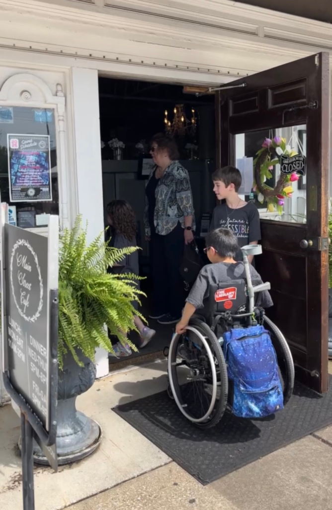 boy in wheelchair rolling through door being held open by his brother