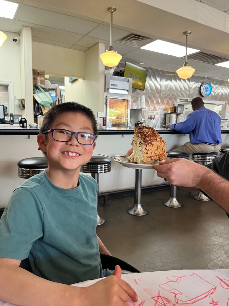 little boy smiling with large piece of pie being held by his head