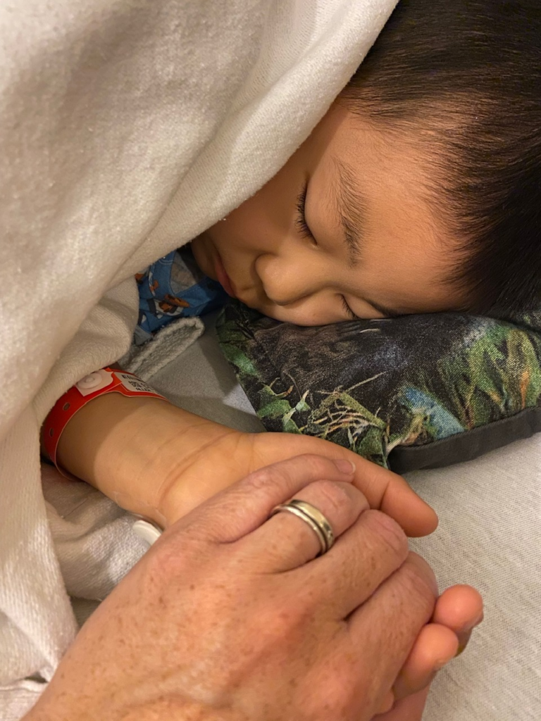 mom holding little boy's hand in hospital bed
