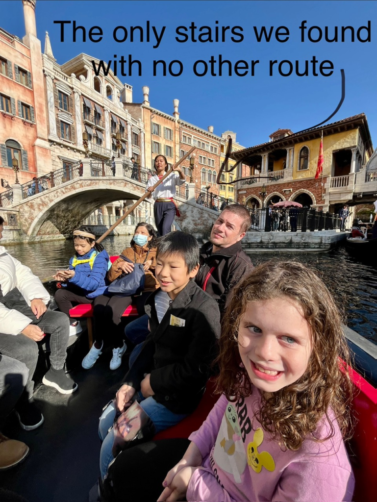 family smiling on gondola in Venice setting. Arrow points to stairs on bridge.