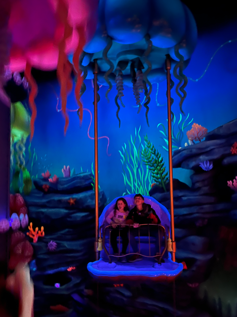 little boy and girl staring at black lit colors on a ride that looks like a jellyfish.