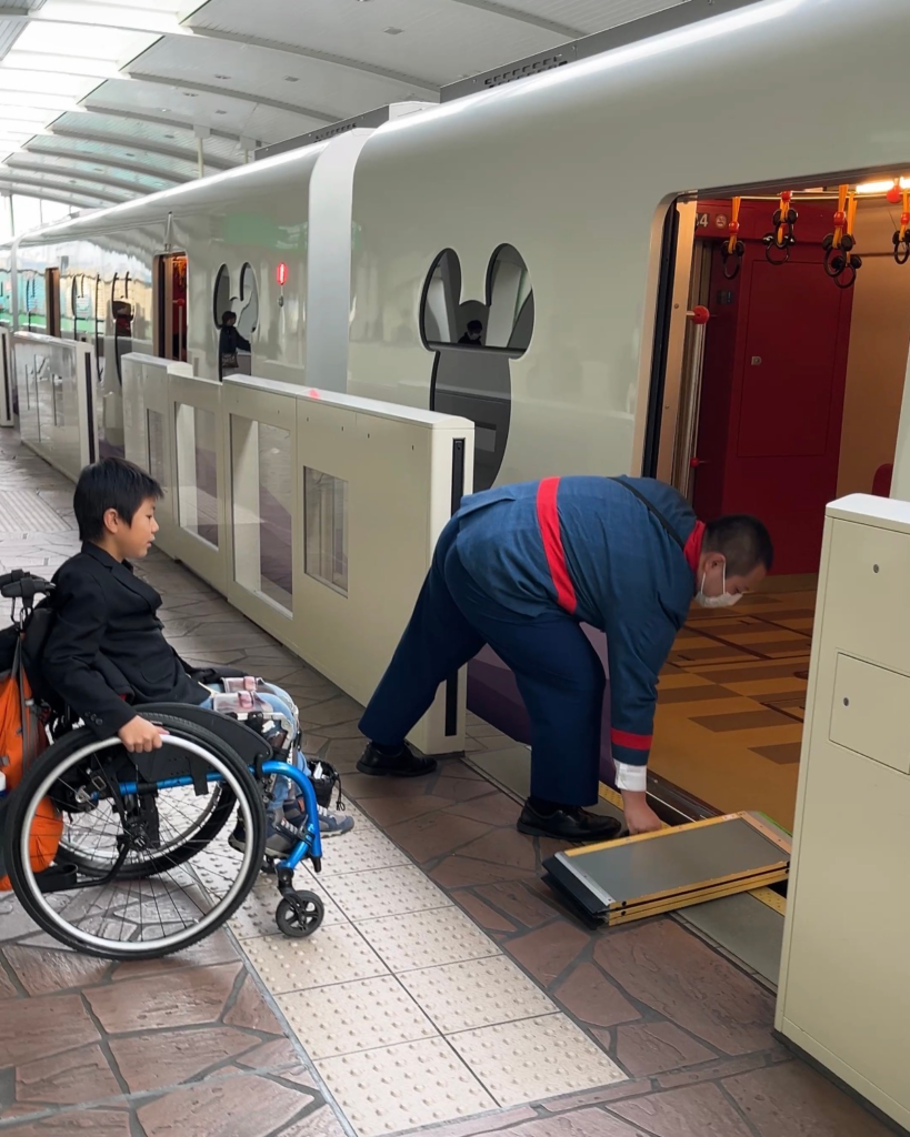 Little boy in wheelchair waits for man to lay ramp over monorail gap. The train has mickey shaped windows.