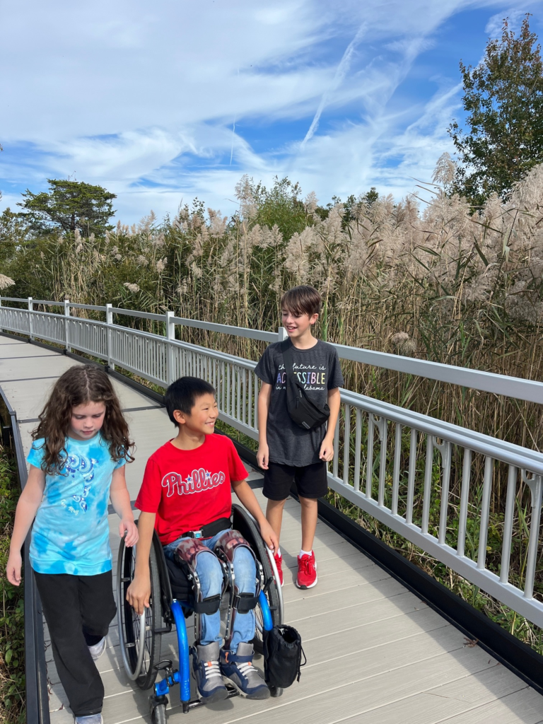 three children, one in a wheelchair, strolling an accessible path and laughing