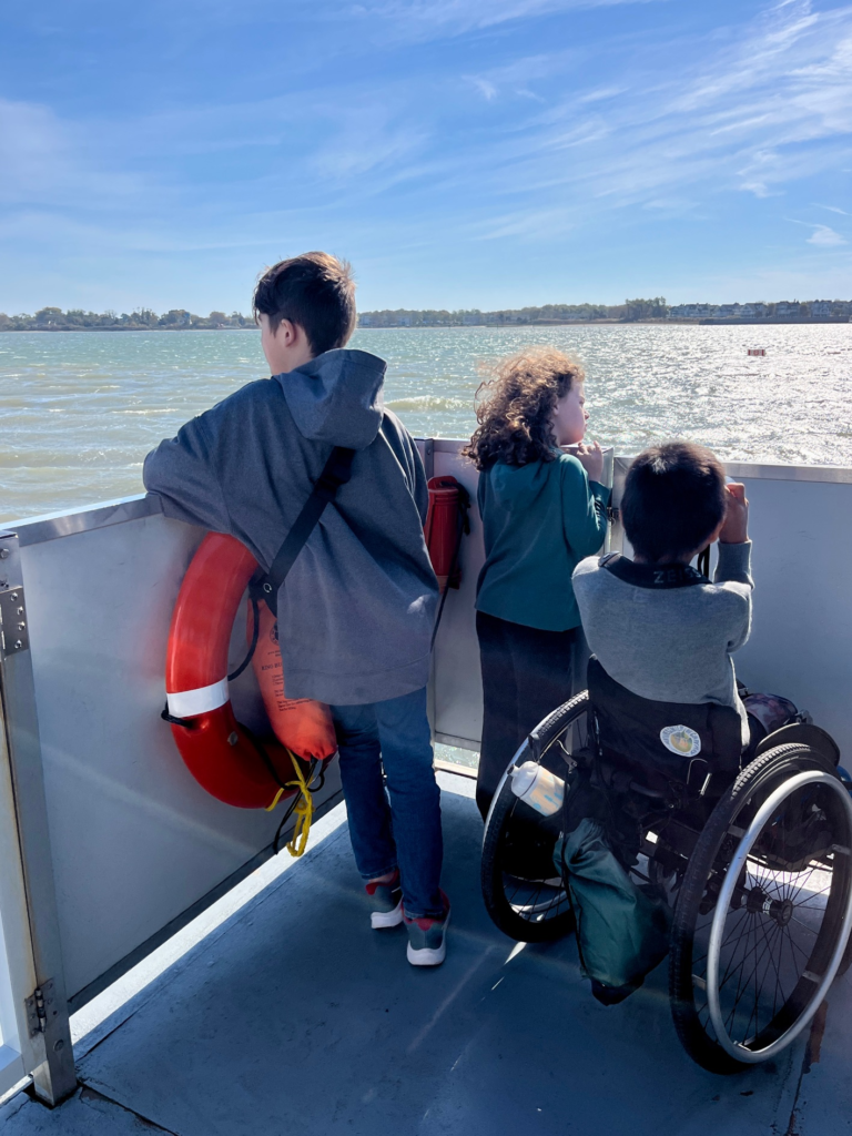 backs of three children as they look out across the ocean from a boat deck