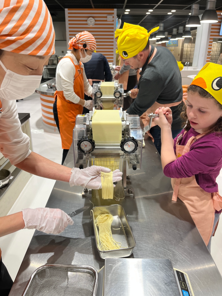little girl focused on rolling noodles as a factory worker helps catch the cut pieces