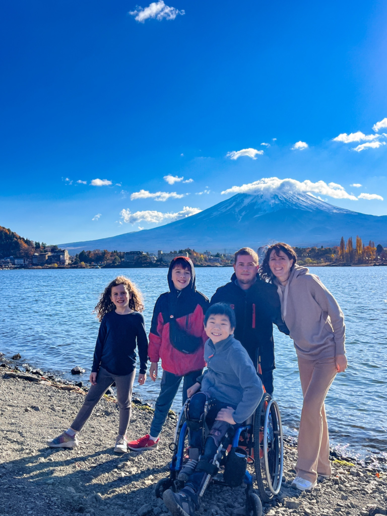 family with two sons, one in a wheelchair, and one daughter, smaile at camera with Mt Fuji in the background behind a lake
