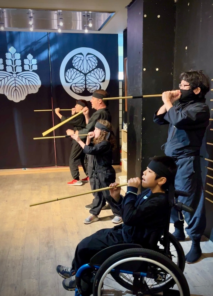 boy in ninja suit in wheelchair holds a blow dart gun up to his mouth
