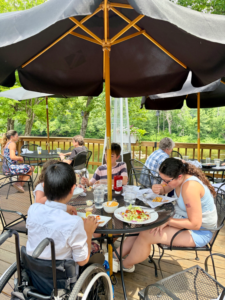 family around picnic table under umbrella with river in the background